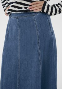 Jeansrok met een hoge taille, met een rechte snit, donkerblauwe kleur en zichtbare stikseldetails. Gedragen met een zwart-wit gestreepte trui.
