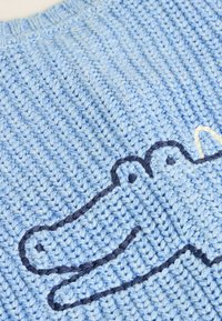 Hellblauer gestrickter Pullover mit einem strukturierten Muster, versehen mit einem dunkelblauen gestickten Krokodildesign und einem kleinen cremefarbenen Akzent darüber.