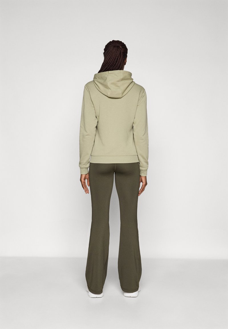 Haut à capuche vert clair avec une grande capuche et des poignets côtelés, associé à des leggings évasés vert olive. Design simple et sans couture. Chaussures blanches.