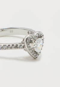 Ασημένιο δαχτυλίδι με κεντρικό διαμάντι σε σχήμα καρδιάς, περιτριγυρισμένο από μικρότερα διαμάντια στη στεφάνη και περίγραμμα καρδιάς.