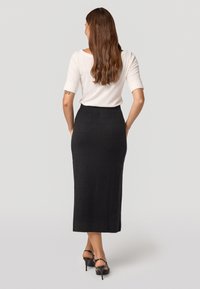 Jupe midi noire avec un motif à carreaux, fabriquée en tissu texturé. Associée à un haut blanc et des sandales à talons noirs.