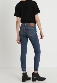Jeans de tiro alto en un azul oscuro, con corte ajustado, que cuentan con un parche de cuero en la parte trasera y un dobladillo ligeramente deshilachado. Combinados con una camiseta negra holgada y botas de tobillo.