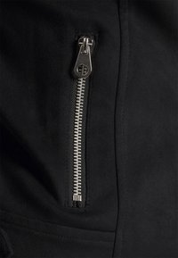 Musta mokkanahkainen takki, jossa näkyvä hopeinen vetoketju vasemmalla puolella, sileä pinta ja virtaviivainen muotoilu.