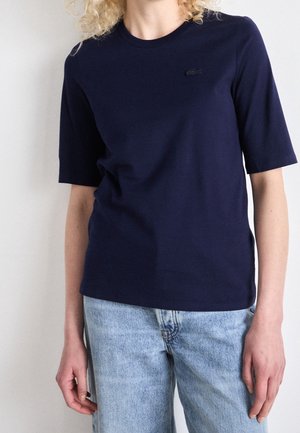 Camiseta de algodón de color azul marino con mangas cortas, cuello redondo y un pequeño logotipo tonal en el pecho. Ajuste casual con un diseño minimalista.
