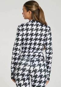 Abbigliamento sportivo con motivo houndstooth in bianco e nero, realizzato in un tessuto liscio e morbido. Presenta maniche lunghe e un design aderente.