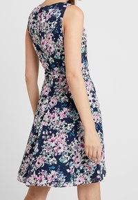 Blommig klänning med marin bakgrund, som har rosa och gröna blommönster, ärmlös design och en utsvängd kjol.