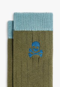 Guantes de punto doblados en verde oliva y azul claro con puños acanalados y un bordado de una calavera y tibias en azul en un guante.