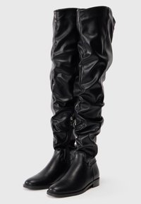 Botas negras de imitación cuero por encima de la rodilla con textura fruncida, cierre de cremallera y tacón plano. Acabado suave con diseño de punta afilada.