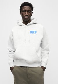 Γκρι φούτερ με κουκούλα, μπροστινή τσέπη, κορδόνι στην κουκούλα και μπλε λογότυπο "OBEY". Ο υφασμάτινος φαίνεται μαλακός, με άνετη εφαρμογή και ριμπ μανσέτες.