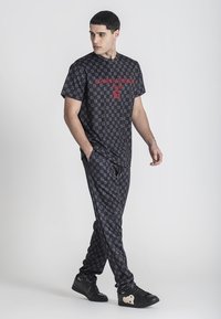 Čierny, vzorovaný outfit pozostávajúci z trička s krátkym rukávom a zodpovedajúcich nohavíc. Tkanina má mriežkový dizajn s červenými logovými akcentmi.