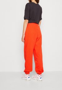 Svart avkortad t-shirt, lös passform. Klara orangea sweatpants, elastisk midja och ärmslut. Vita sneakers med röda och blå detaljer.