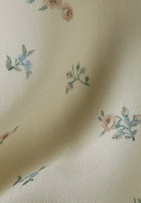 Beige tyg med en subtil texturväv, dekorerad med små pastellblommiga mönster i blå, rosa och gröna nyanser.