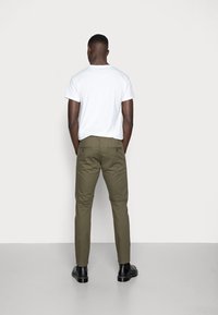 Olivgröna byxor med slim fit, med bakfickor med knappar, i kombination med en figurnära vit t-shirt och svarta skor.