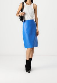 Modrá kožená tužková sukně s hladkým povrchem, kombinovaná s přiléhavým bílým žebrovaným tílkem a černými kotníkovými ponožkami, doplněná špičatými černými podpatky.