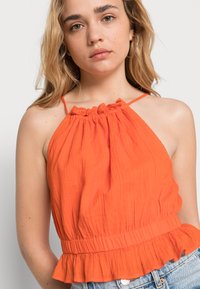 Top halter laranja feito de tecido leve com uma bainha franzida e decote gathered, apresentando alças finas e um ajuste descontraído.