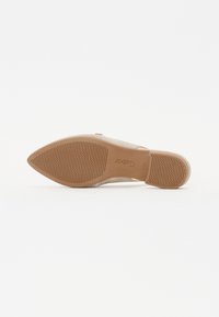 Beige flat shoe with a pointed toe, fabric upper, and a textured rubber sole featuring a honeycomb pattern. Embossed logo near the heel.