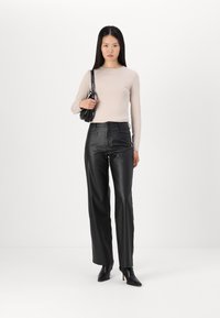 Lichtbeige langsl sleeve met hoge taille zwarte leren broek en zwarte hoge enkellaarsjes. Een kleine zwarte handtas is als accessoire toegevoegd.