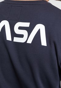 Sweatshirt bleu marine avec un grand logo "NASA" blanc au dos, fabriqué en tissu doux, avec col rond et une texture subtile.