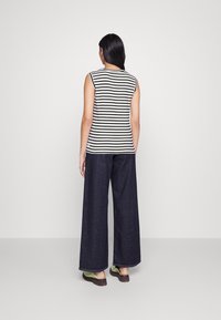 Top sin mangas a rayas en blanco y negro, combinado con pantalones de mezclilla anchos de color azul oscuro. Acabado con sandalias verdes.