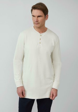 Langsleeve, crème kleurige shirt met een ronde halslijn en drie gouden knopen aan de voorkant, met een gladde katoentextuur.