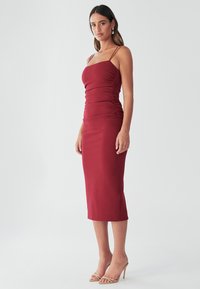 Burgundské přiléhavé midi šaty s nařasenou strukturou, tenkými ramínky a výstřihem do oblouku, doplněné o tělové sandály na podpatku.