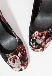Paire de ballerines en velours noir avec motifs floraux multicolores, présentant des bouts arrondis et des semelles intérieures lisses sur fond blanc.