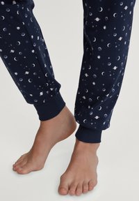 Marineblauwe pyjamabroek met een hemels patroon van manen, planeten en sterren, voorzien van elastische boorden bij de enkels en een zachte textuur.