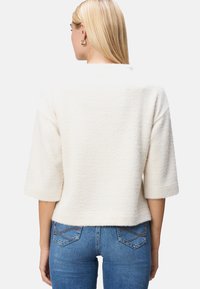 Hvid hørfransk mønstret sweater med 3/4 ærmer og en afslappet pasform, parret med tætsiddende blå jeans. Blød tekstur og struktureret design.