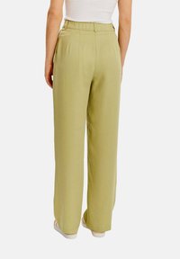 Kalhoty s širokými nohavicemi v jasně olivově zelené barvě, s vysokým pasem, záhyby a hladkou texturou látky. Zadní pohled ukazuje čisté linie a minimální detaily.