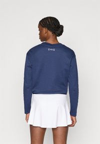 Μπλε ναυτικό μακρυμάνικο φούτερ με λευκό λογότυπο στην πλάτη, σε συνδυασμό με λευκή φουσκωτή φούστα. Μαλακό ύφασμα με άνετη εφαρμογή.