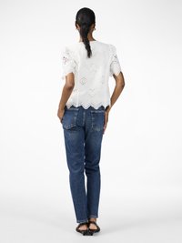 White broderie anglaise top with puff sleeves, scalloped hem; paired with mid-rise blue denim jeans and black heeled sandals.