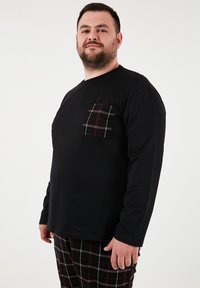 Sort langermet skjorte med enternet lomme; parret med ternede pyjamabukser. Stoffet ser blødt og behageligt ud.