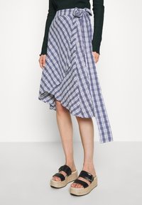 Blå och vit randig omlottkjol med en ojämn fåll och en sidobåge, i kombination med svarta platåsandaler med spänne.