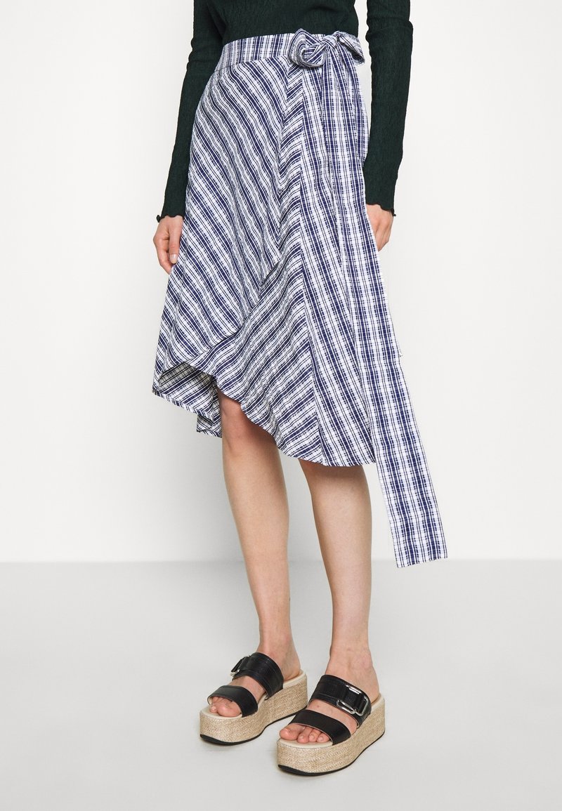 Blå och vit randig omlottkjol med en ojämn fåll och en sidobåge, i kombination med svarta platåsandaler med spänne.