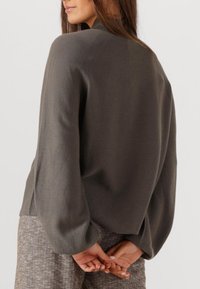 Grauer Strickpullover mit hohem Kragen, entspannter Passform und leicht ausgestellten Ärmeln. Glatte Textur und minimalistische Designmerkmale.