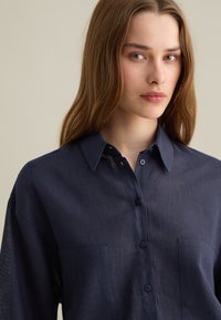 Navy blue, long-sleeve button-up shirt made of lightweight fabric, featuring a collar, two chest pockets, and a relaxed fit.
