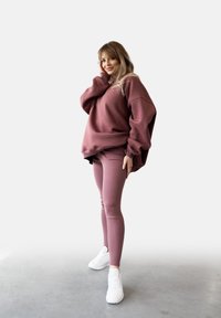 Przestronna maroon bluza z kapturem i dopasowane legginsy, obie z miękkiego, elastycznego materiału. Białe sneakersy dopełniają swobodny wygląd.