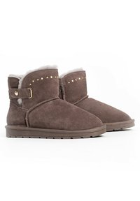 Botas de tobillo de ante marrón con un suave forro de piel blanca, tachuelas doradas decorativas y una correa con una hebilla dorada. Suela de goma plana.