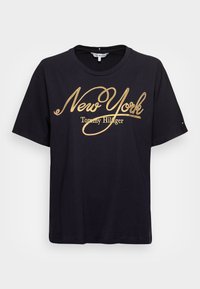 Schwarzes Baumwoll-T-Shirt mit kurzen Ärmeln. Mit "New York" in goldener Schrift und dem Text "Tommy Hilfiger". Design mit Rundhalsausschnitt.