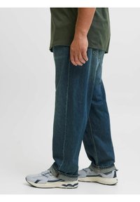 Blauwe denim jeans met een losse fit, gestikte details en een licht grijzige rand, gecombineerd met grijze sport schoenen.
