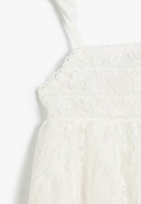 Abito bianco in pizzo con delicati motivi floreali, texture a strati, spalline regolabili e bordi ondulati. Materiale morbido e leggero.
