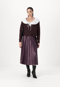 Pulover tricotat roșu-maroniu cu un guler alb cu volane, asortat cu o fustă pliată violet și cizme negre până la genunchi. Este inclusă o geantă de mână neagră.