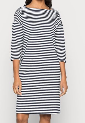 Femme portant une robe rayée horizontale noir et blanc longueur genou avec des manches trois-quarts et un décolleté bateau.