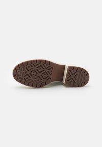 Brown rubber outsole with a textured geometric pattern, featuring a beige midsole and a durable construction for traction and stability.