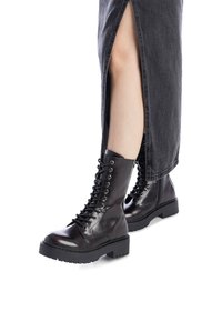 Botas negras de cuero con cordones, punta redonda, suela gruesa y detalles de ojales, combinadas con una falda de mezclilla gris que presenta una abertura lateral.