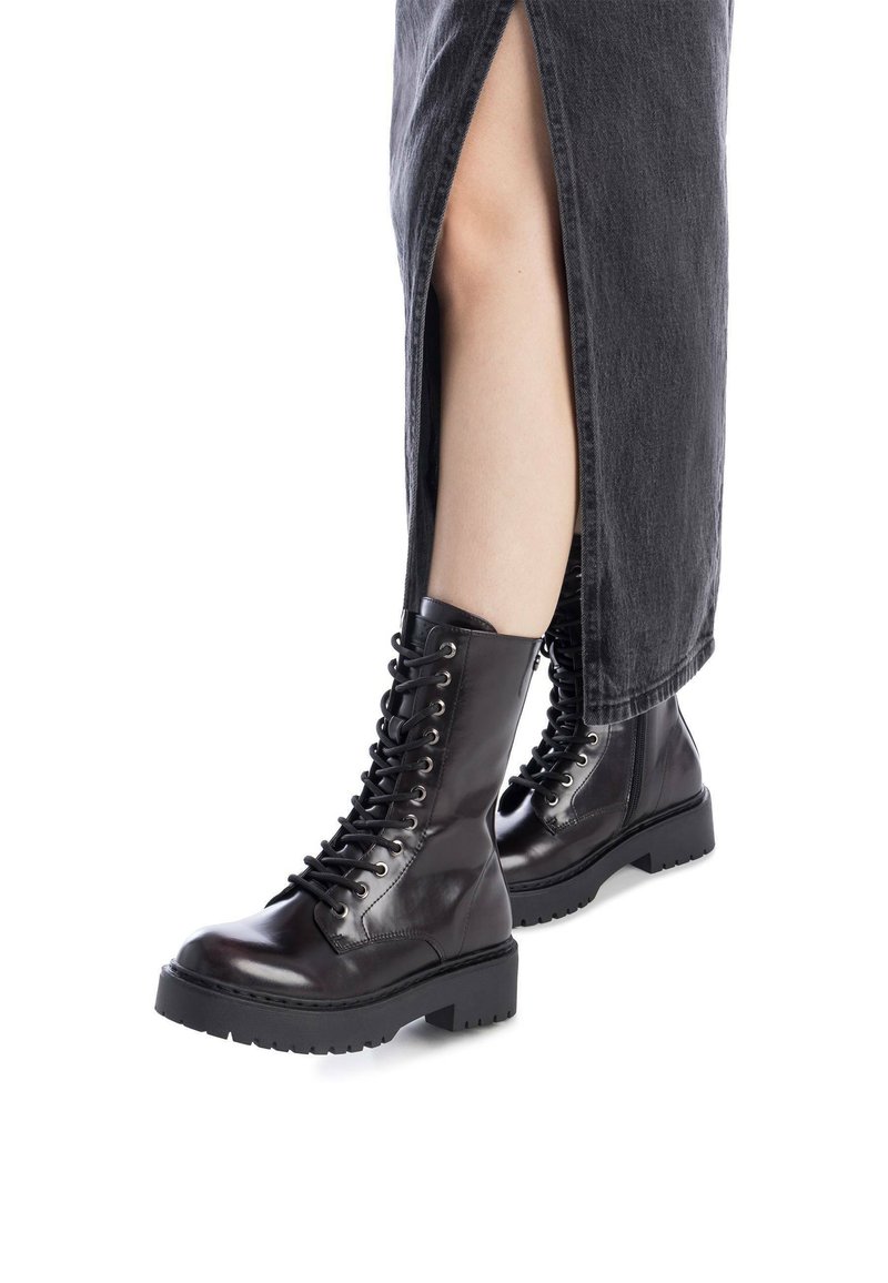 Botas negras de cuero con cordones, punta redonda, suela gruesa y detalles de ojales, combinadas con una falda de mezclilla gris que presenta una abertura lateral.