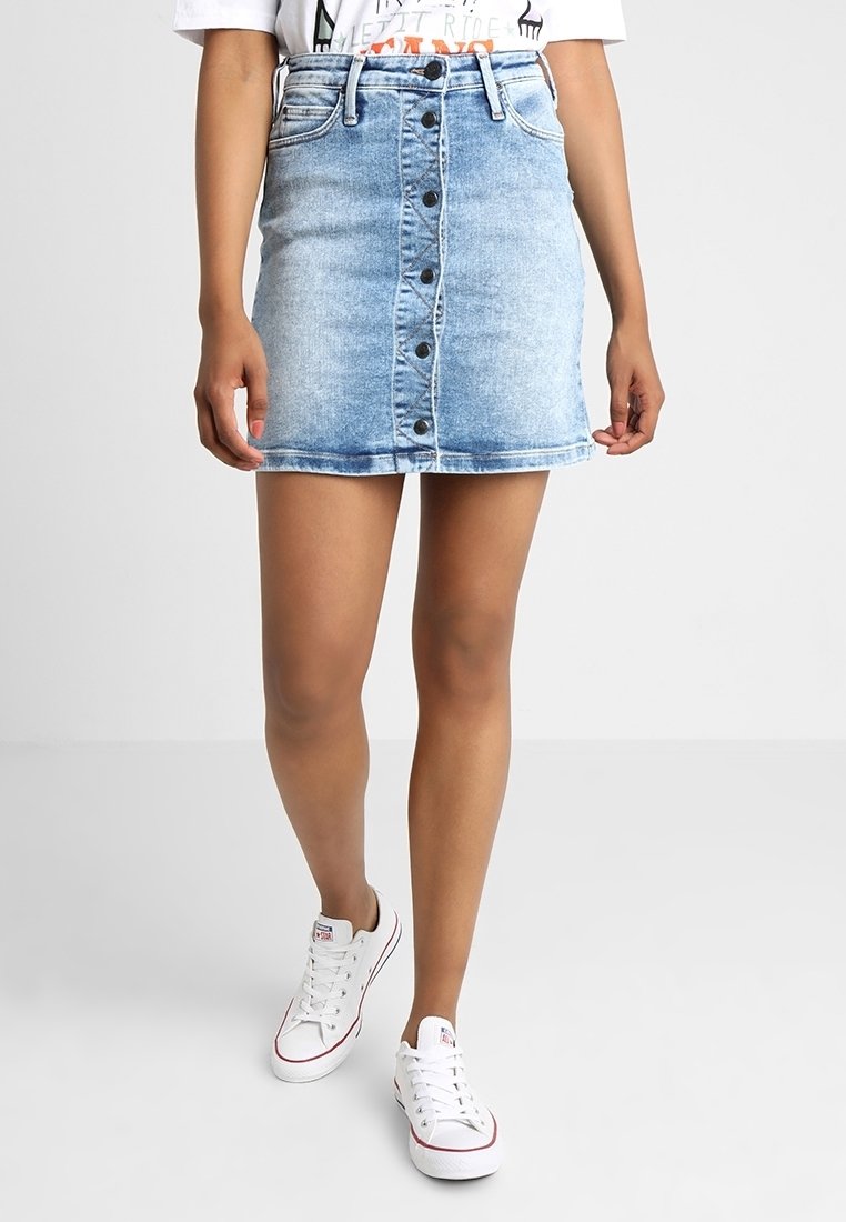 Džínová sukně v světle modré barvě s přiléhavým střihem, předními knoflíky a třepeným lemem. V kombinaci s bílými teniskami.