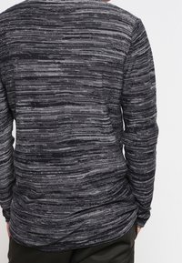 Haut à manches longues en gris foncé avec un motif à rayures horizontales texturé. Tissu doux avec une coupe décontractée et un col rond.