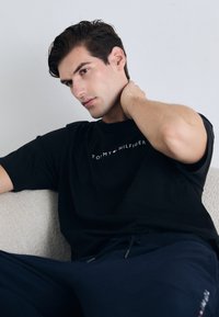 Schwarzes Baumwoll-T-Shirt mit dem Grafikdesign "TO MY HILFIGER" in Weiß, kombiniert mit marineblauen Jogginghosen. Weicher Stoff, lässige Passform, Rundhalsausschnitt.