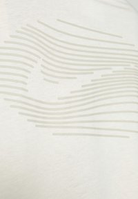 Vit bomull t-shirt med subtila, böjda grå linjer tryckta i varierande bredder över tygets yta. Slät textur.